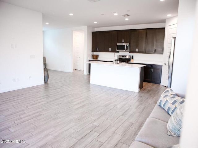 kitchen with dark brown cabinetry, appliances with stainless steel finishes, light hardwood / wood-style floors, and a center island with sink