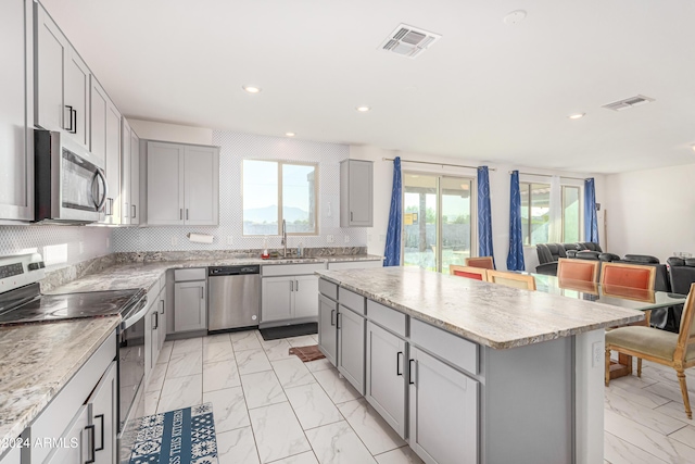 kitchen featuring appliances with stainless steel finishes, a kitchen island, gray cabinetry, and sink