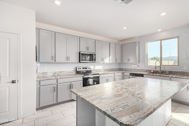 kitchen featuring a center island, sink, gray cabinets, light stone countertops, and stainless steel appliances