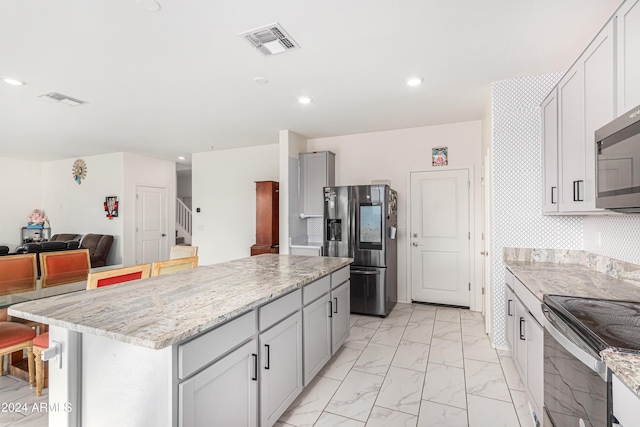 kitchen with a center island, stainless steel appliances, and light stone counters