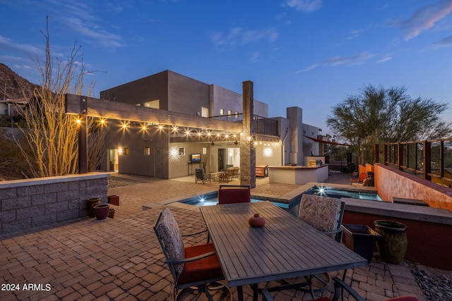 patio terrace at dusk featuring pool water feature and an outdoor kitchen