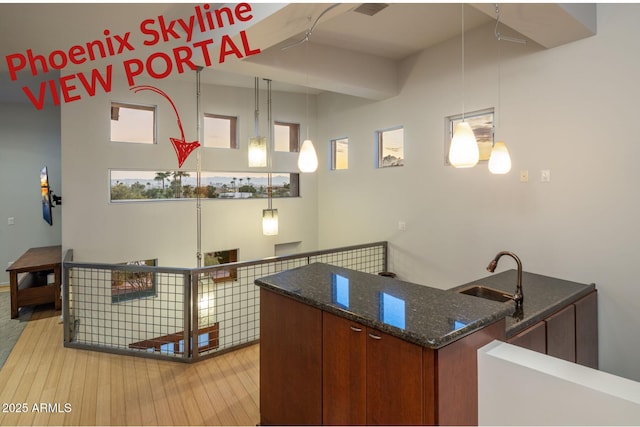 kitchen featuring dark stone countertops, sink, decorative light fixtures, and light hardwood / wood-style flooring