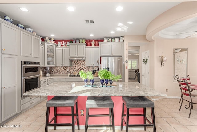 kitchen with light tile patterned floors, a breakfast bar area, stainless steel appliances, under cabinet range hood, and visible vents