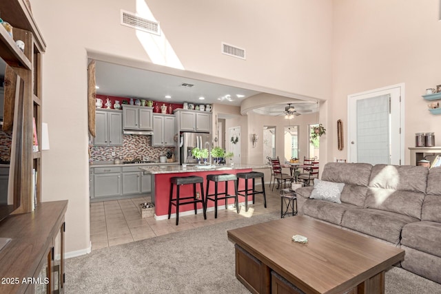living room with ceiling fan, a high ceiling, and visible vents