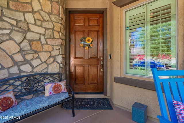 view of exterior entry with stucco siding, a porch, and stone siding