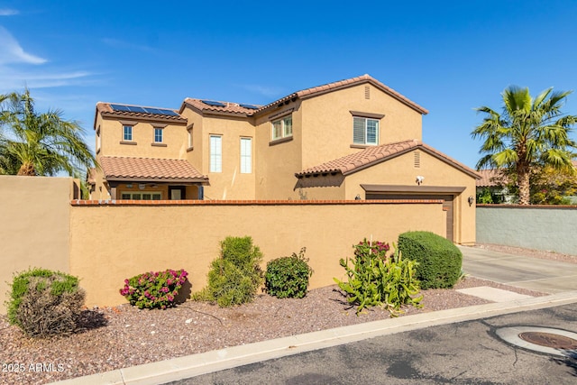 mediterranean / spanish-style house featuring stucco siding, a tile roof, driveway, and a fenced front yard