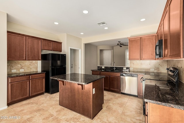 kitchen featuring a sink, a center island, black appliances, dark stone countertops, and a kitchen bar