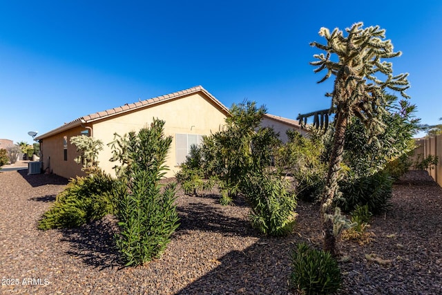 view of side of property with a tile roof, fence, cooling unit, and stucco siding