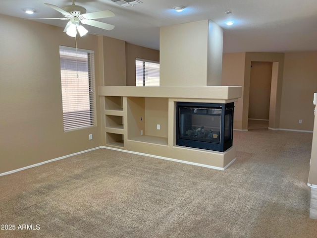 unfurnished living room featuring ceiling fan, a multi sided fireplace, and carpet