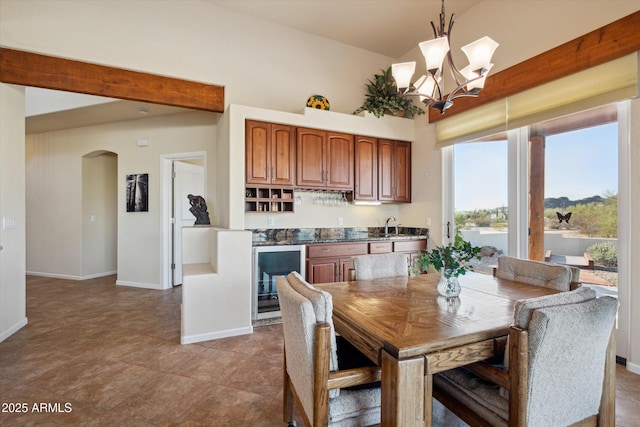 tiled dining space with baseboards, wine cooler, arched walkways, a notable chandelier, and a sink