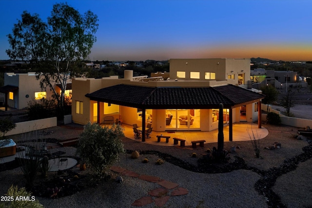 back of house at dusk with stucco siding, a patio, and a tile roof