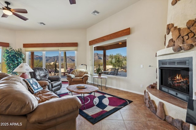 tiled living room featuring a ceiling fan, baseboards, visible vents, a lit fireplace, and a mountain view