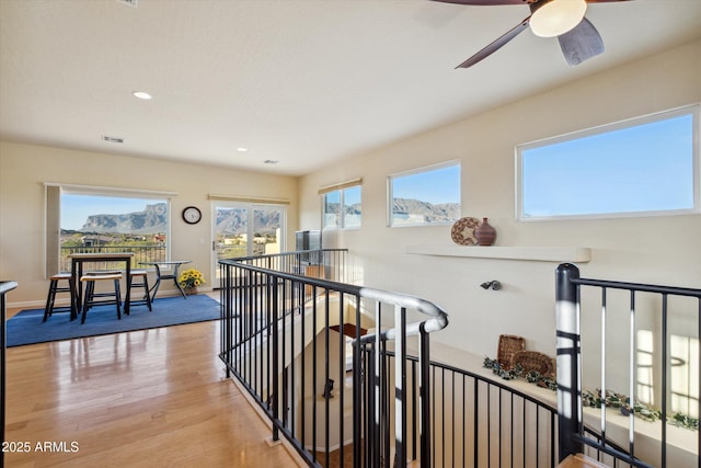 hallway featuring an upstairs landing, visible vents, light wood-style flooring, and a wealth of natural light