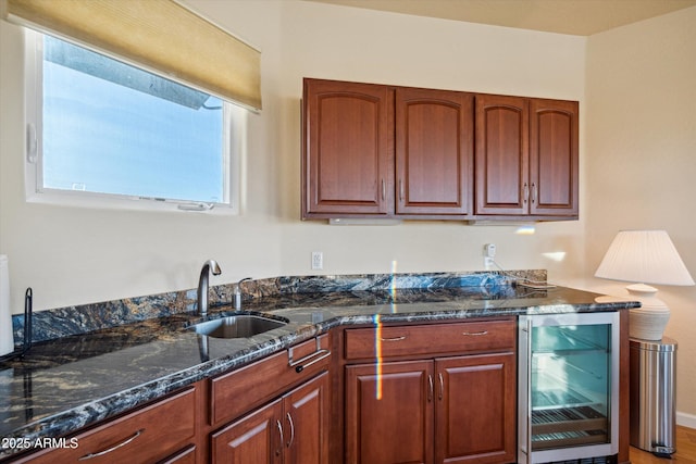 kitchen featuring dark stone countertops, beverage cooler, and a sink