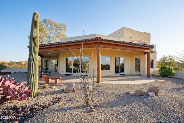 rear view of property with a patio, a tile roof, and stucco siding