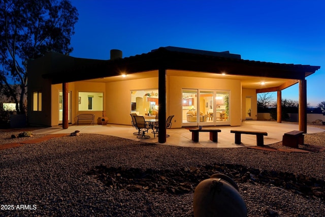 back of house at twilight with stucco siding, a tile roof, and a patio