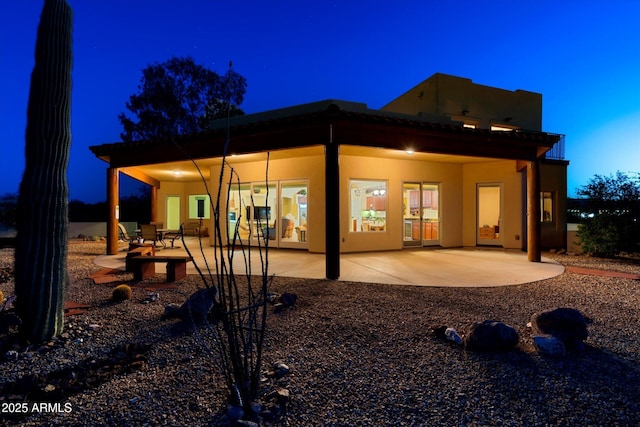 back of house at night with a patio and stucco siding