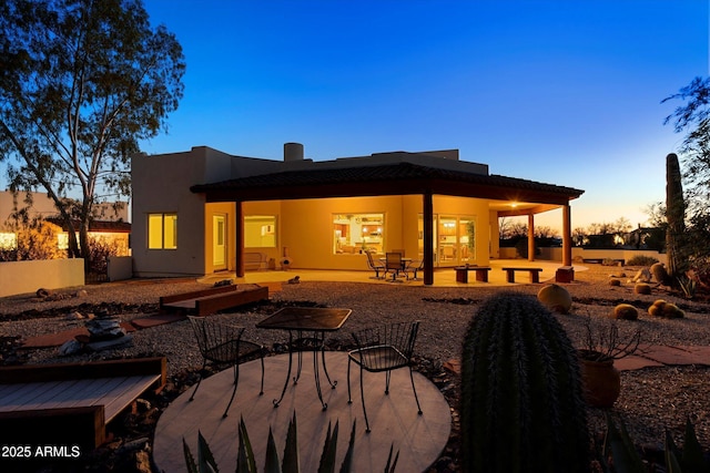 back of property at dusk with a patio area and stucco siding