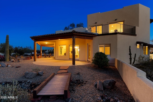 back of house featuring a balcony, a patio area, and stucco siding