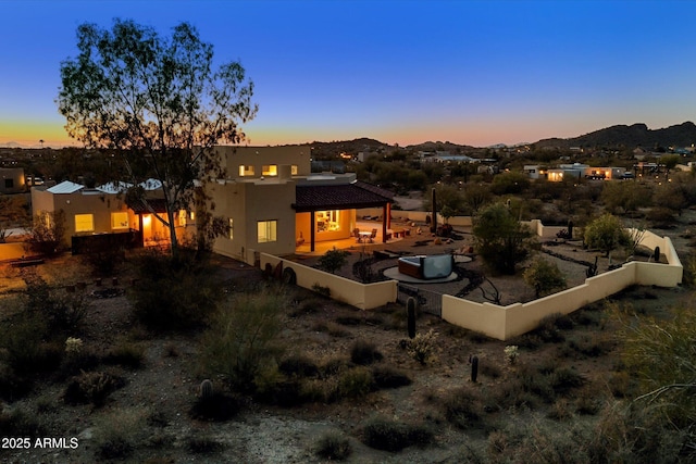 back of house at dusk with stucco siding, a patio, and fence