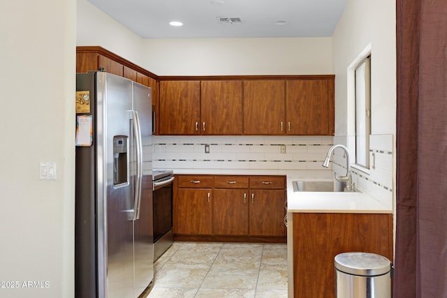 kitchen with appliances with stainless steel finishes, a sink, decorative backsplash, brown cabinetry, and light countertops