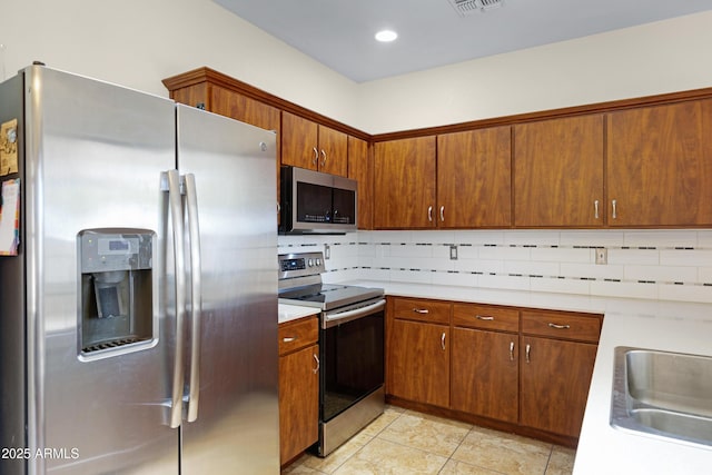 kitchen featuring stainless steel appliances, tasteful backsplash, light countertops, a sink, and brown cabinets