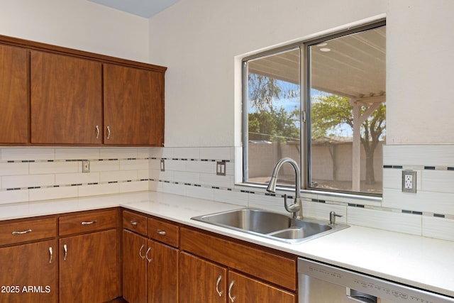 kitchen featuring stainless steel dishwasher, a sink, backsplash, light countertops, and brown cabinets