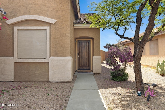 property entrance with stucco siding, fence, and a tiled roof