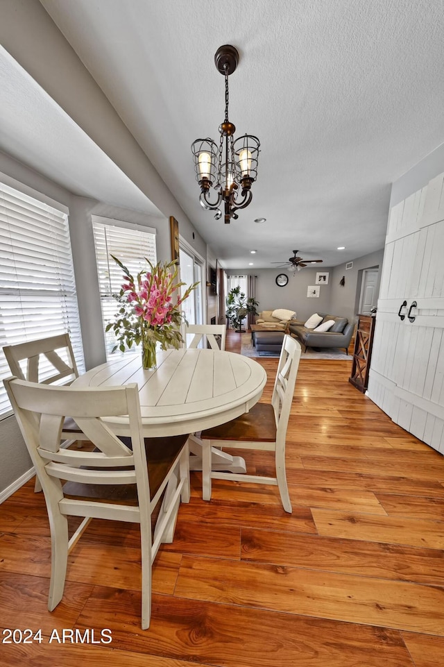 dining area featuring hardwood / wood-style floors, ceiling fan with notable chandelier, and a textured ceiling