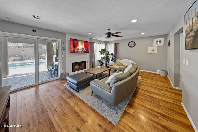 living room with a large fireplace, light hardwood / wood-style flooring, a textured ceiling, and ceiling fan