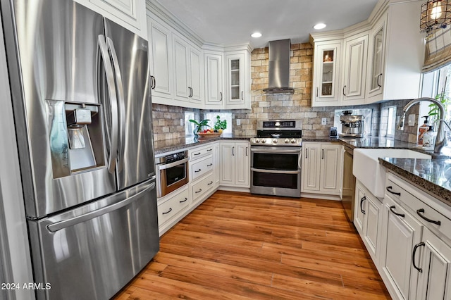 kitchen featuring stainless steel appliances, sink, light hardwood / wood-style flooring, white cabinets, and wall chimney range hood