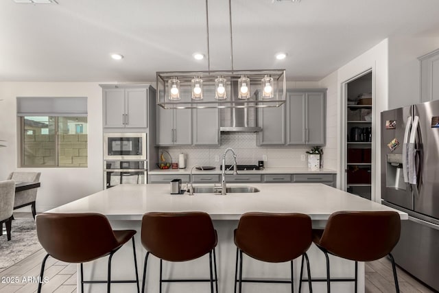 kitchen featuring gray cabinets, decorative backsplash, light hardwood / wood-style floors, stainless steel appliances, and a center island with sink