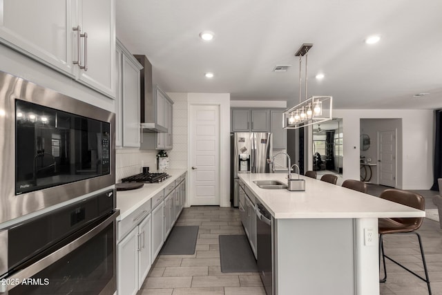 kitchen with a breakfast bar area, backsplash, gray cabinetry, stainless steel appliances, and a center island with sink