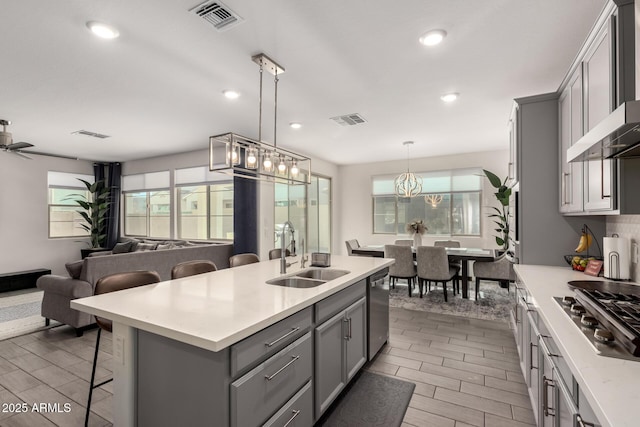 kitchen featuring sink, a kitchen bar, a kitchen island with sink, stainless steel appliances, and wall chimney exhaust hood