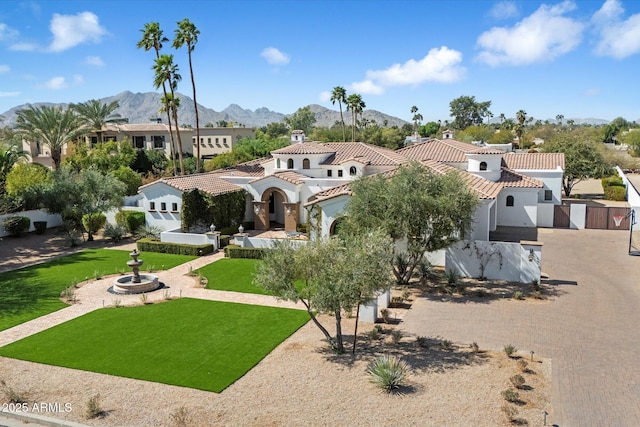 mediterranean / spanish-style house with a mountain view, fence, a tiled roof, stucco siding, and a front lawn