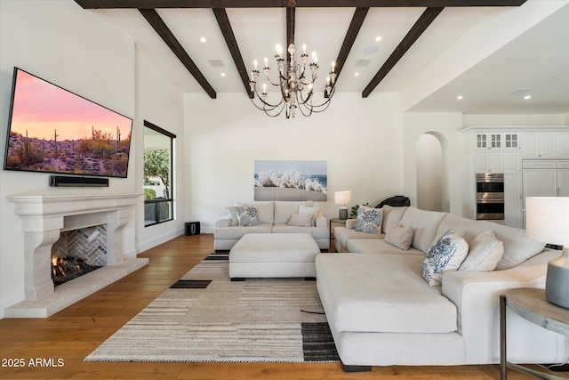 living area featuring arched walkways, a warm lit fireplace, wood finished floors, visible vents, and beamed ceiling