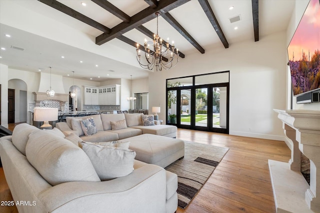 living area featuring light wood-type flooring, visible vents, arched walkways, and beamed ceiling