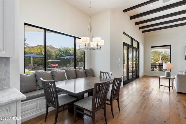 dining area with light wood-type flooring, a towering ceiling, beam ceiling, and french doors