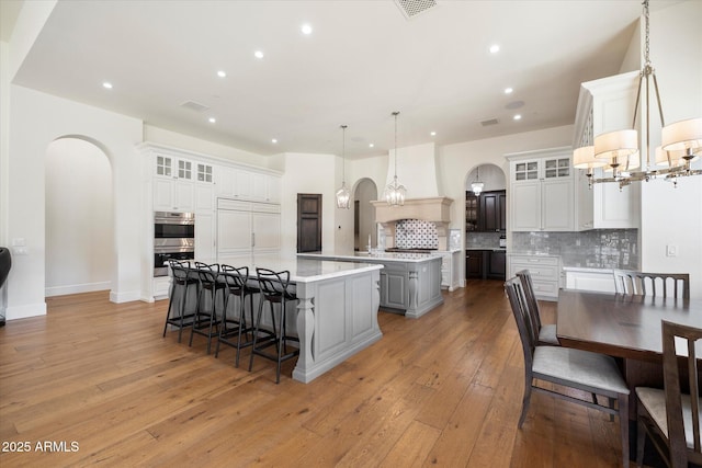 kitchen with arched walkways, stainless steel double oven, custom exhaust hood, a large island with sink, and an inviting chandelier