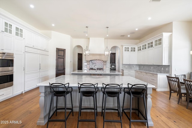 kitchen with arched walkways, double oven, a spacious island, light wood-type flooring, and custom range hood