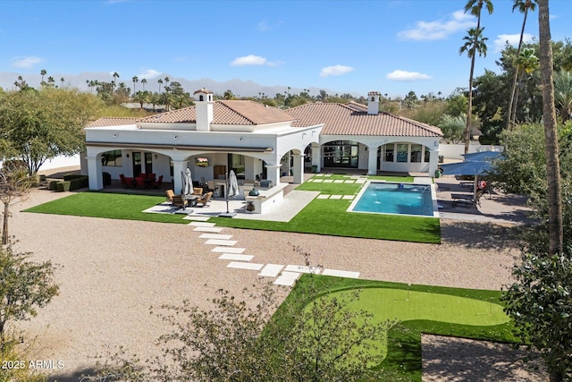 rear view of house with an outdoor pool, a tile roof, stucco siding, a chimney, and a patio area