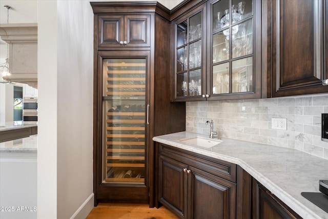 bar featuring beverage cooler, a sink, light wood-style floors, decorative backsplash, and indoor wet bar