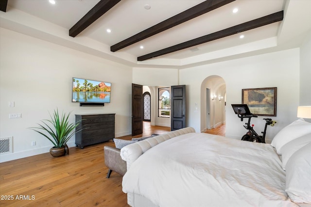 bedroom with light wood-type flooring, baseboards, arched walkways, and beam ceiling