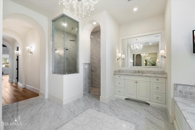 full bathroom featuring an inviting chandelier, baseboards, walk in shower, and vanity