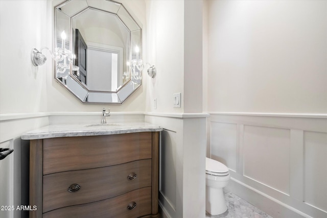 half bathroom with toilet, a wainscoted wall, a decorative wall, and vanity