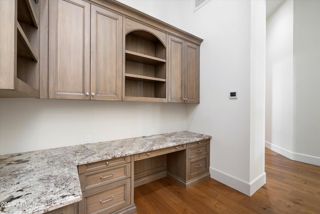 unfurnished office with dark wood-type flooring, visible vents, built in desk, and baseboards