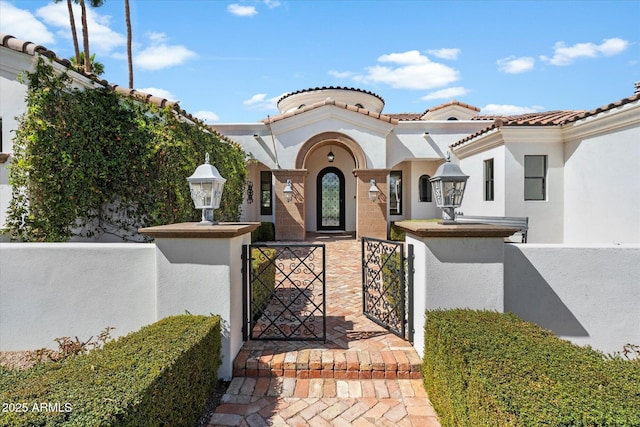 view of front of property featuring a fenced front yard, a gate, a tiled roof, and stucco siding