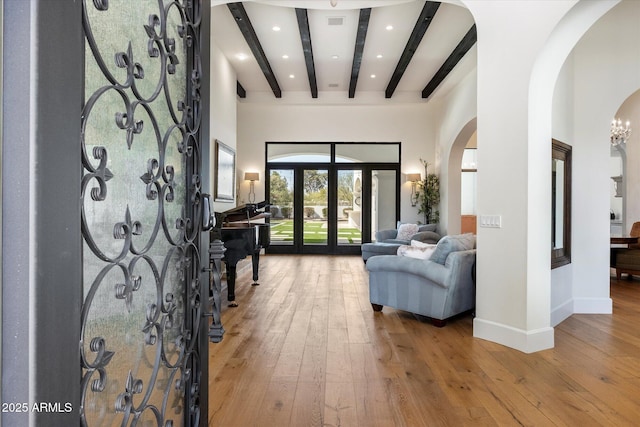 foyer featuring baseboards, arched walkways, wood-type flooring, french doors, and beam ceiling