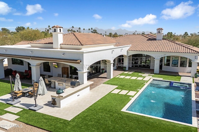 back of property featuring a chimney, outdoor dry bar, a lawn, and a patio