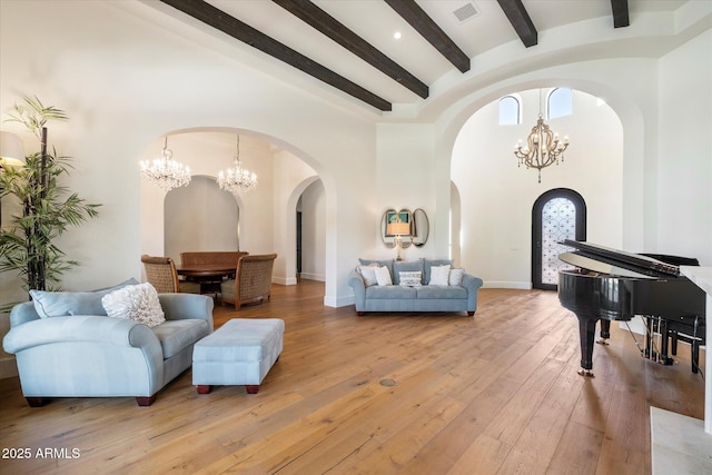 living area with arched walkways, visible vents, a towering ceiling, an inviting chandelier, and light wood-style floors